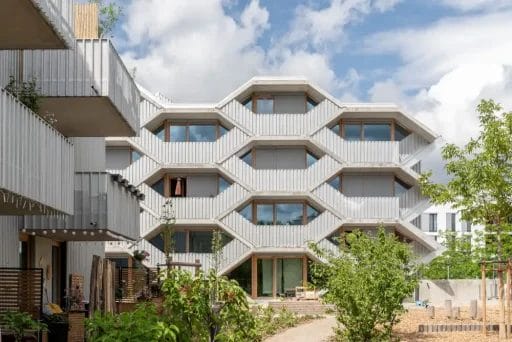 Seitenansicht des Wabenhauses. Davor und seitlich befinden sich grüne Sträucher und kleine Bäume.