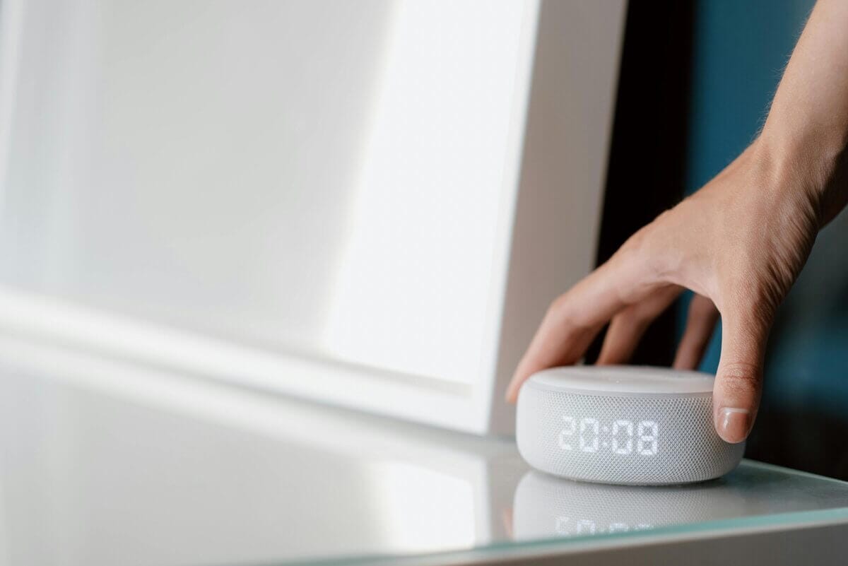 Hand auf smartem Lautsprecher mit digitaler Uhranzeige.